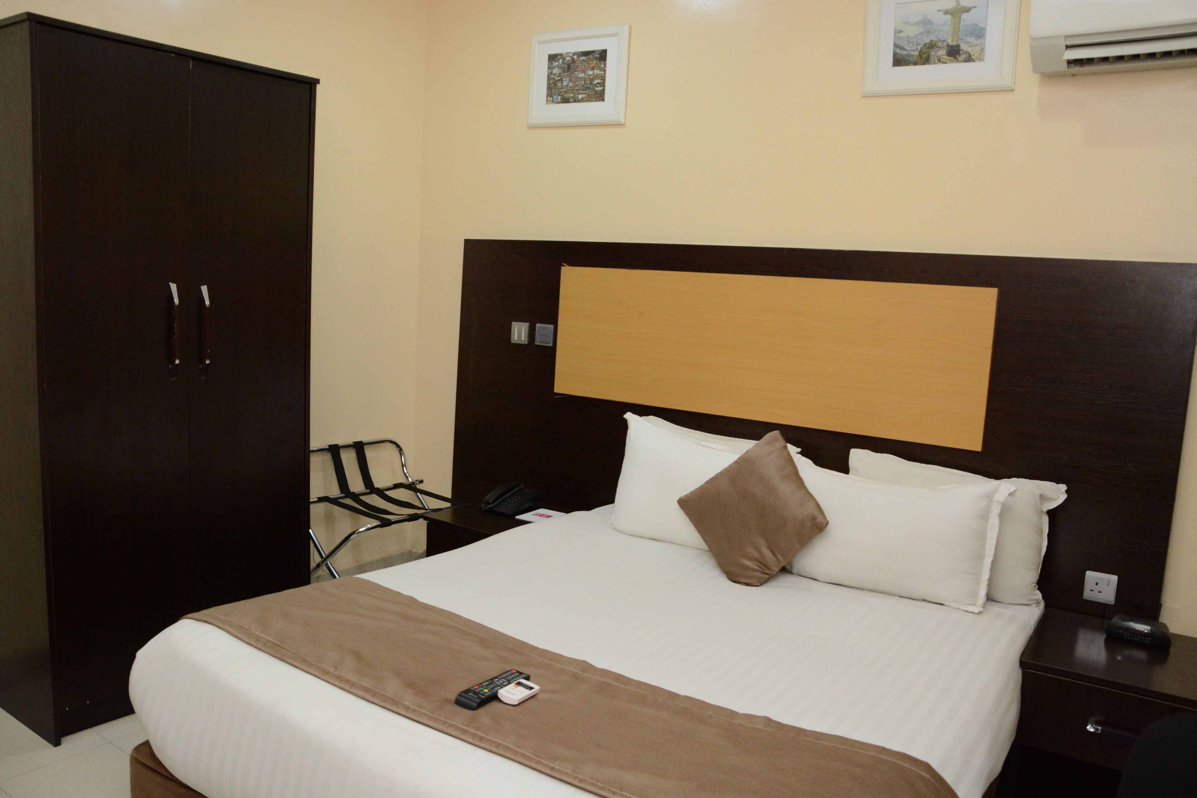 Habitación de hotel con una cama grande, un armario, una mesita de noche con teléfono y una pequeña mesa con una silla.