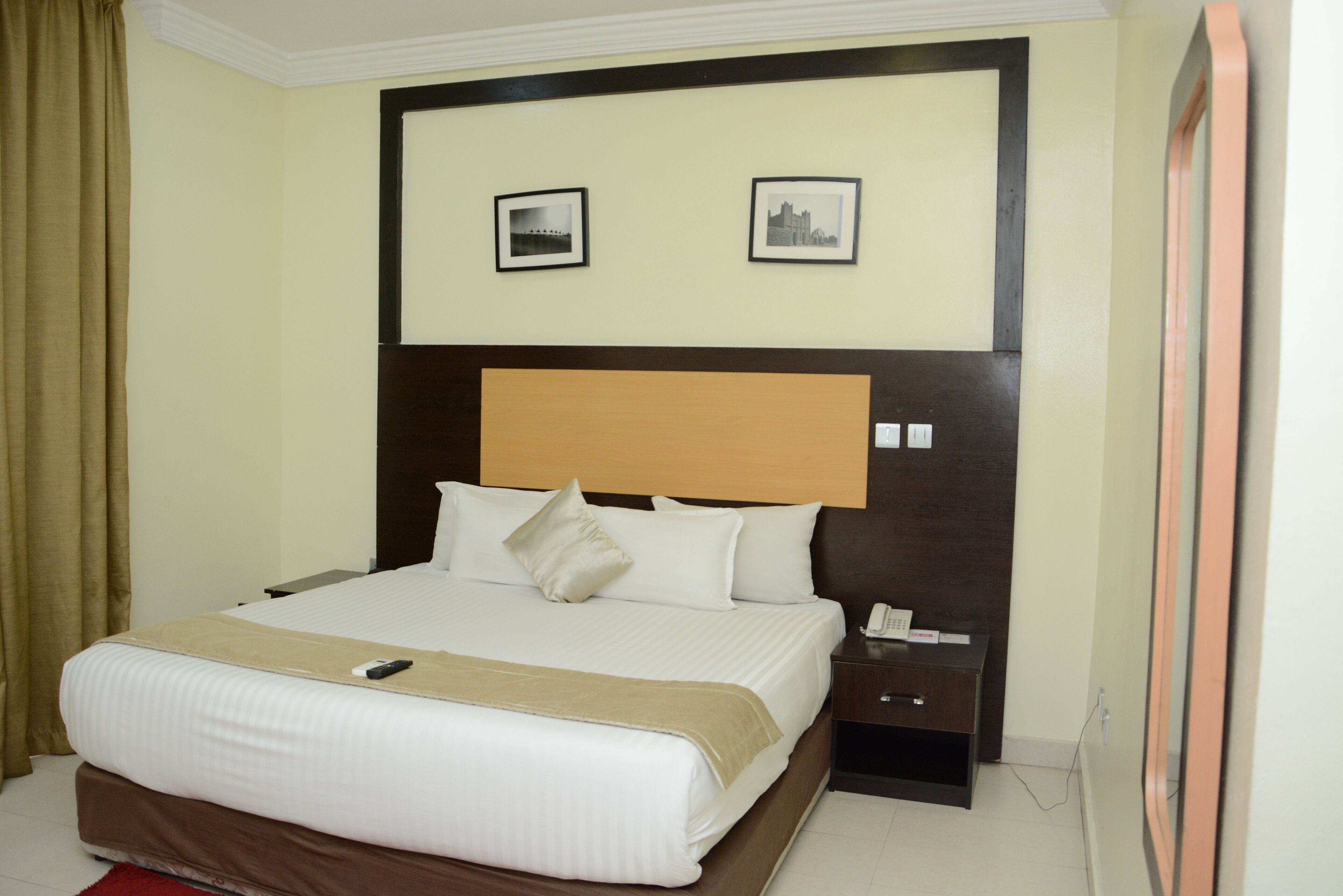 A hotel room with a large bed, a bedside table with a phone, and two framed pictures on the wall.