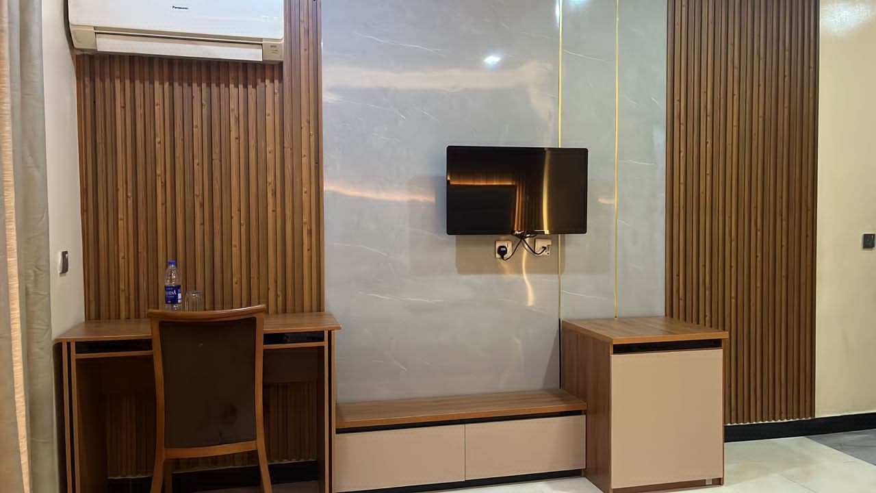 A modern room with a flat-screen TV mounted on a wall, a wooden desk with a chair, and a small cabinet.