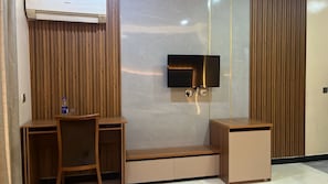 A modern room with a flat-screen TV mounted on a wall, a wooden desk with a chair, and a small cabinet.