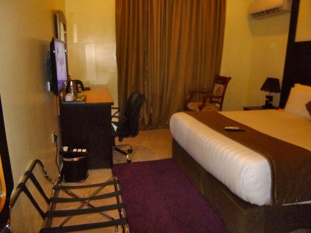 Een hotelkamer met een bed, een bureau, een stoel, een televisie en een raam met gordijnen.