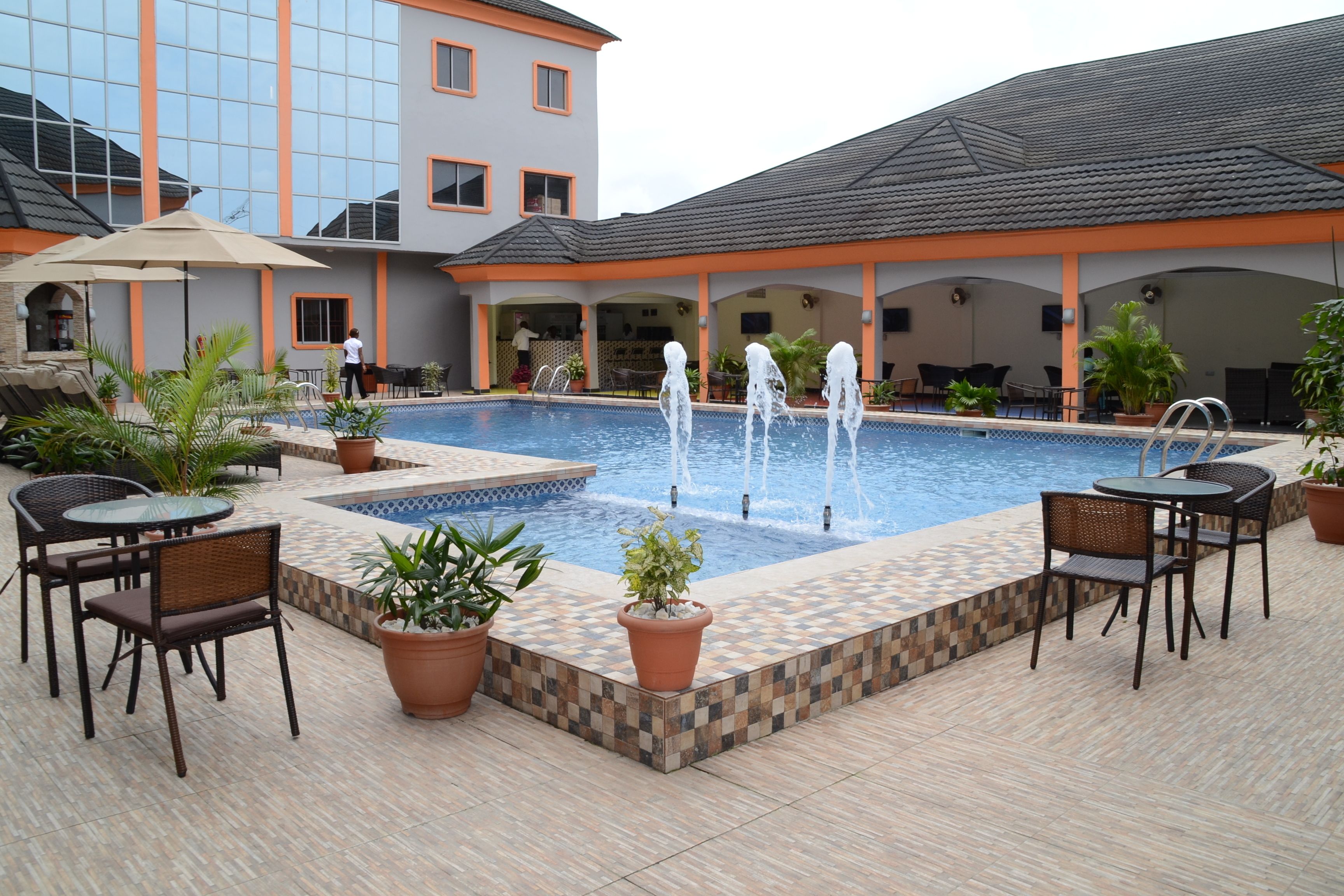 A swimming pool with a fountain, surrounded by outdoor seating and potted plants.