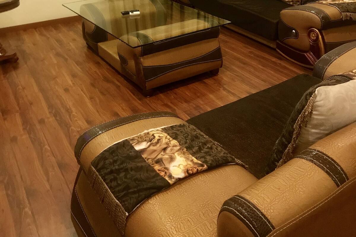 Een woonkamer met een glazen salontafel, leren banken en een groen gordijn.