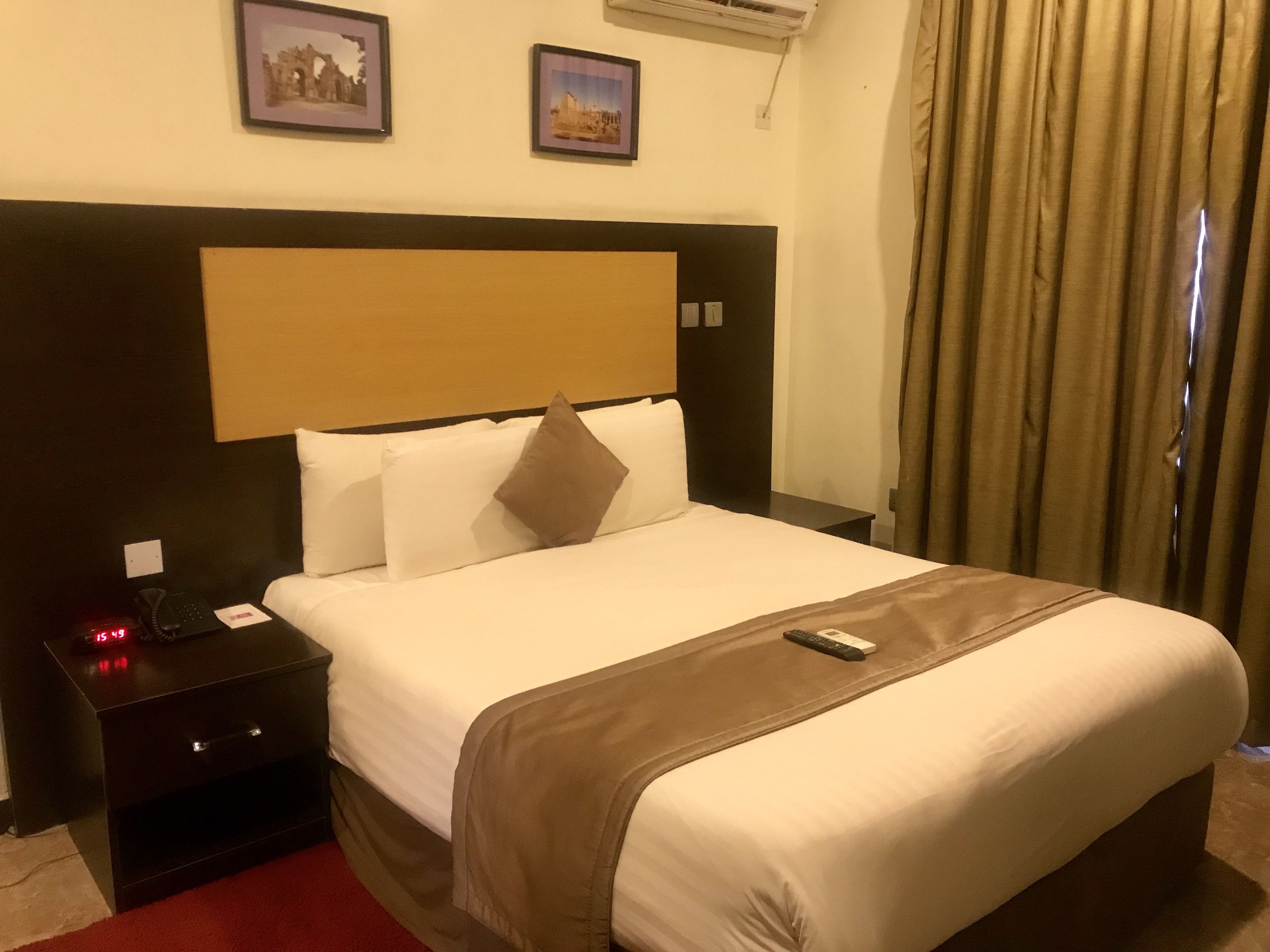 A hotel room with a large bed, a bedside table with a phone, and a remote control on the bed.