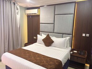 A hotel room with a bed, a nightstand, an air conditioning unit, and a curtain. - Warri Wetland Hotel (Ovwian)