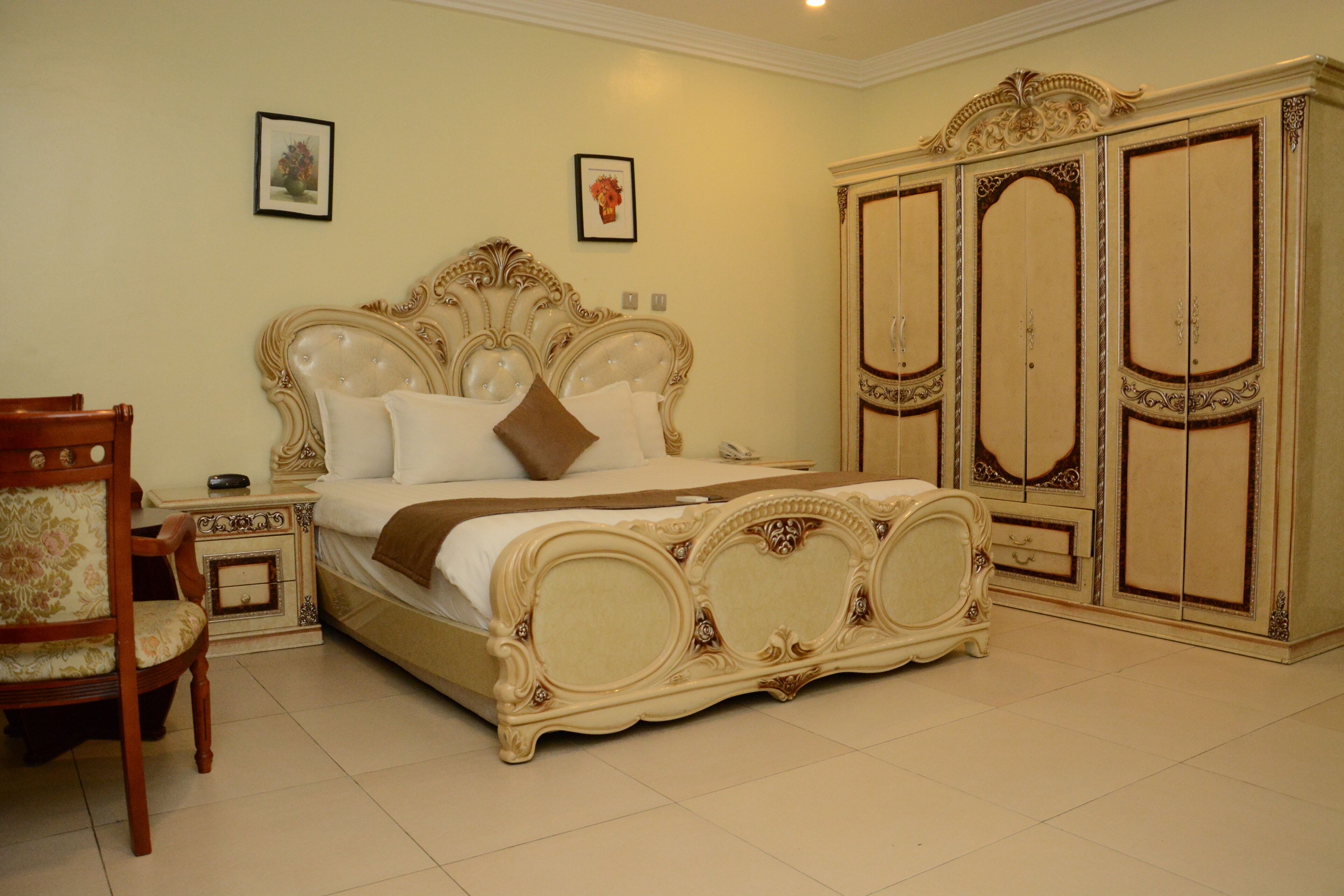 A bedroom with a large bed, a wooden chair, a nightstand, and a wardrobe.
