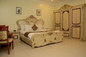 Een slaapkamer met een groot bed, een houten stoel, een nachtkastje en een kledingkast.