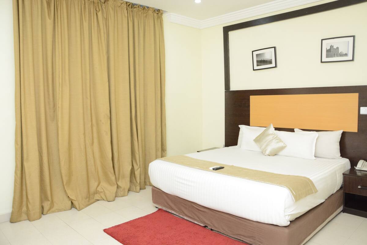 Een hotelkamer met een groot bed, een houten hoofdbord, twee ingelijste foto's aan de muur en een rood vloerkleed.