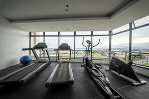 A gym with treadmills, an elliptical, and a stationary bike, large windows with a city view. - Best Western Plus Hotel Subic (Olongapo)
