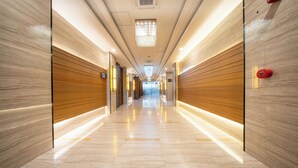 A modern hotel corridor with a polished marble floor, wooden paneling on the walls, and a central chandelier. - Best Western Plus Hotel Subic (Olongapo)