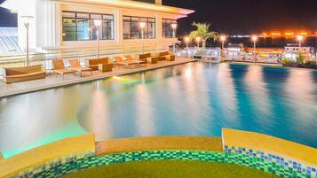 A swimming pool with lounge chairs and a tiled edge, surrounded by a building with large windows and outdoor lighting.