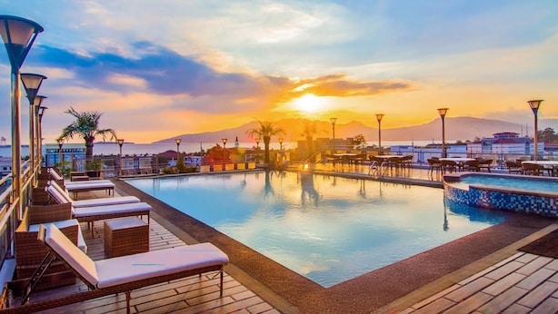 A poolside area with lounge chairs and tables, a sunset view, and a mountain in the background. - Best Western Plus Hotel Subic (Olongapo)