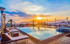A poolside area with lounge chairs and tables, a sunset view, and a mountain in the background. - Best Western Plus Hotel Subic (Olongapo)
