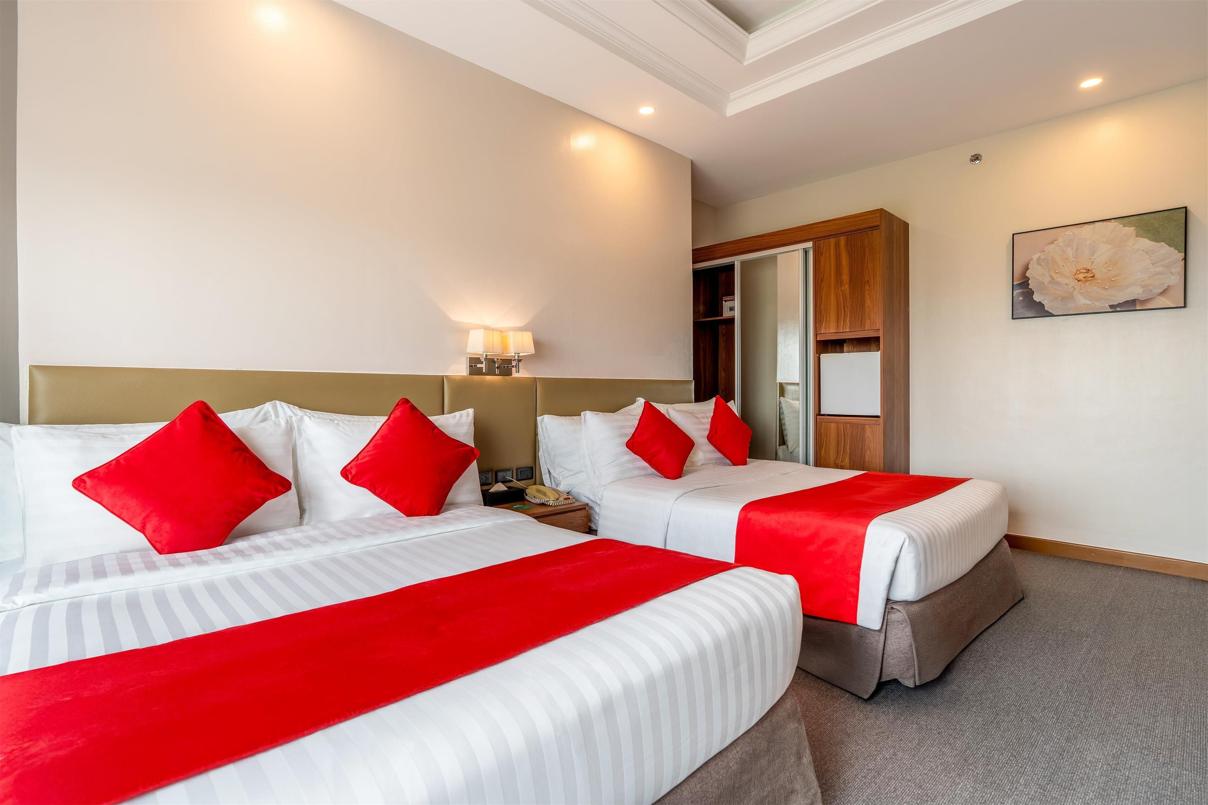 Une chambre d’hôtel avec deux lits, chacun agrémenté de linge de lit blanc et de touches de couleur rouge, une lampe de chevet, une armoire en bois et un grand tableau abstrait accroché au mur.