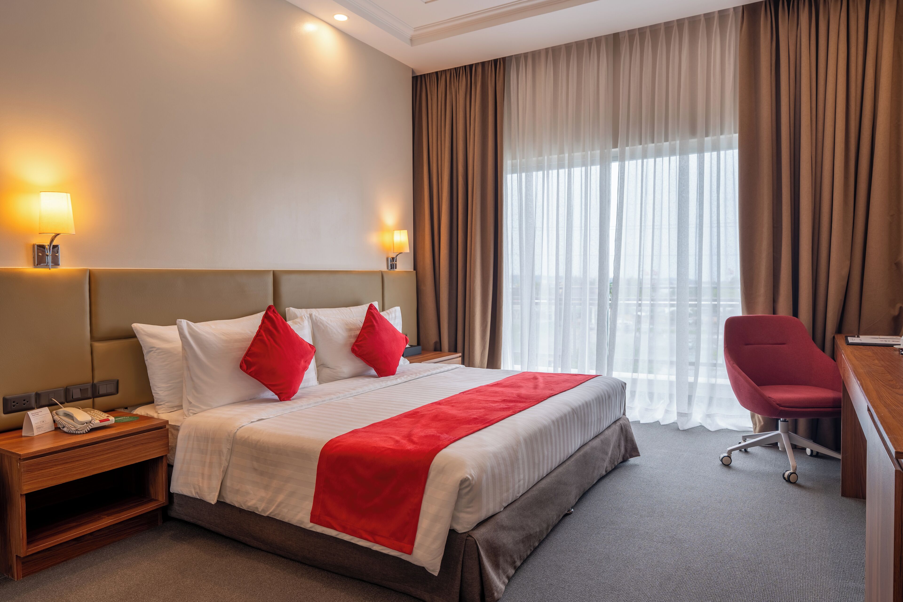 A hotel room with a large bed, a desk, a chair, and a window with curtains.