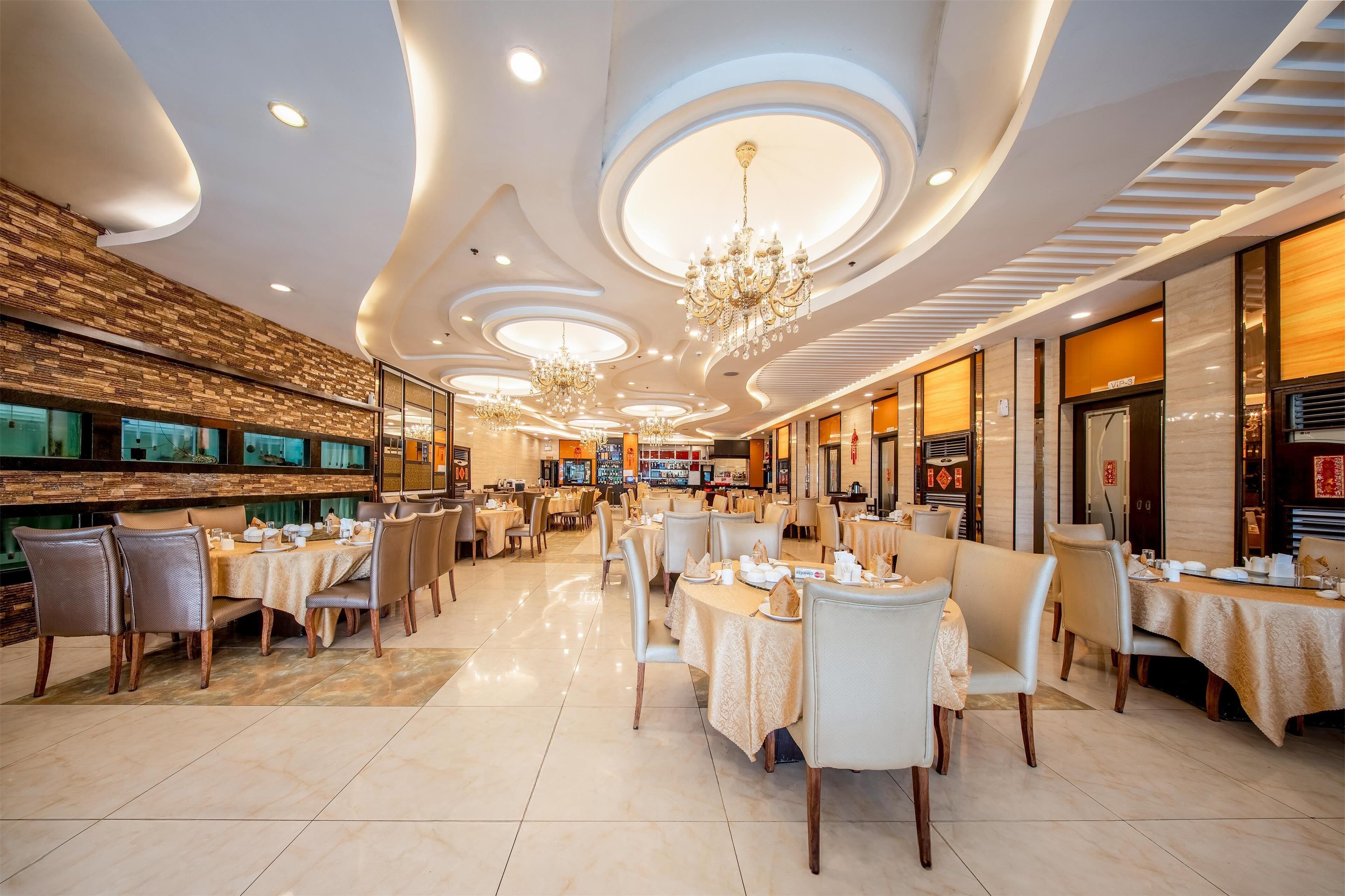 A spacious restaurant with multiple dining areas, chandeliers, and a modern ceiling design.