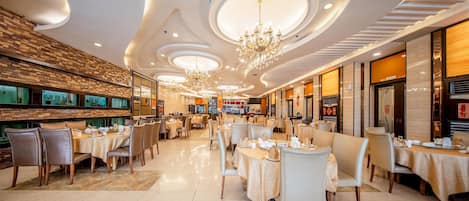A spacious restaurant with multiple dining areas, chandeliers, and a modern ceiling design.