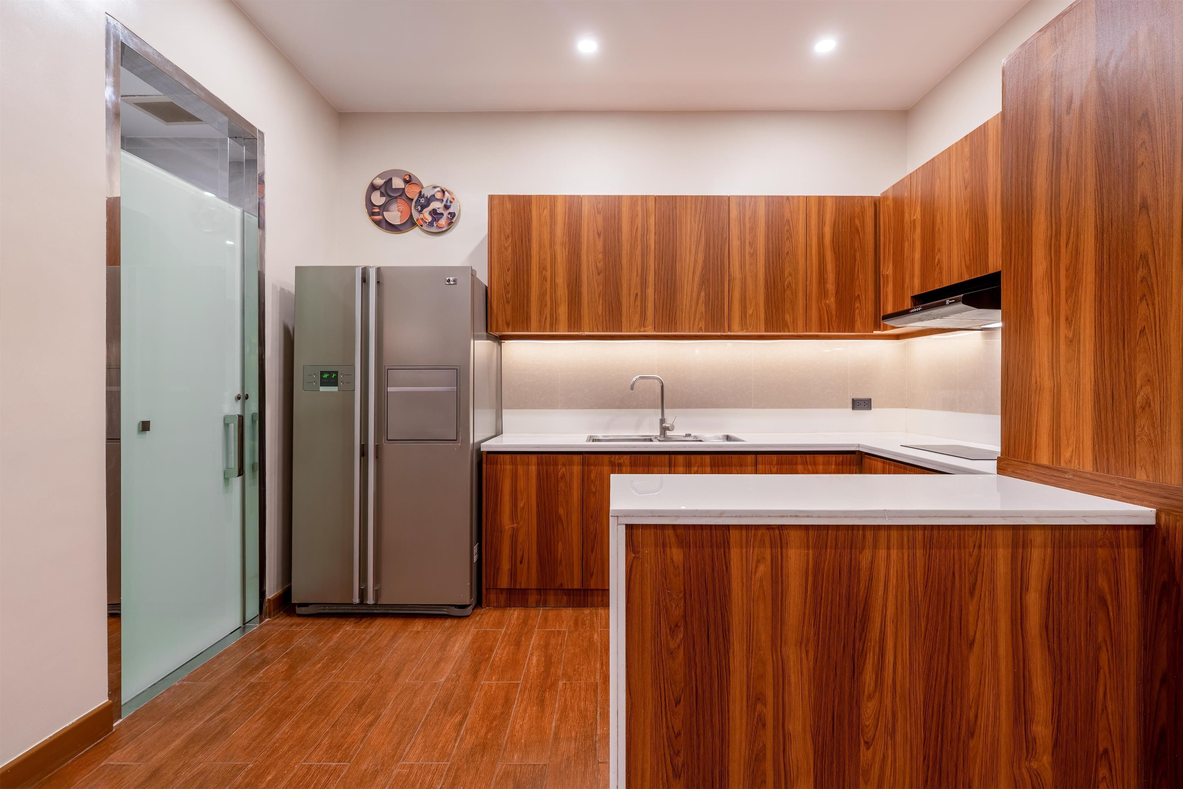 Une cuisine moderne avec des meubles en bois, un réfrigérateur en acier inoxydable et un plan de travail blanc.