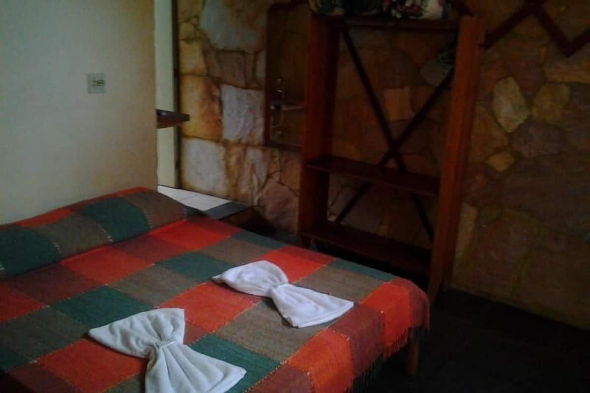 Una habitación con una cama cubierta por una colcha a cuadros, un armario de madera y una pared de piedra.