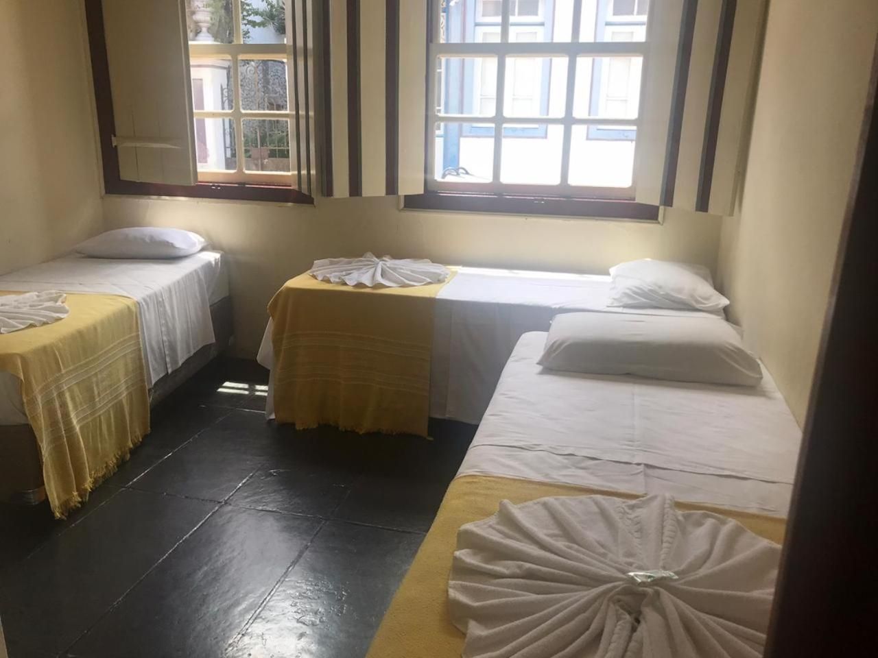 A room with two single beds, a small table, and a window with a view of buildings.