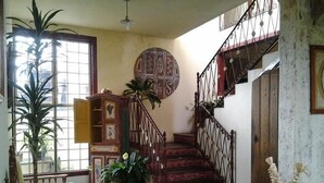 A staircase with ornate metal railings, a wooden cabinet with decorative panels, and a large potted plant.