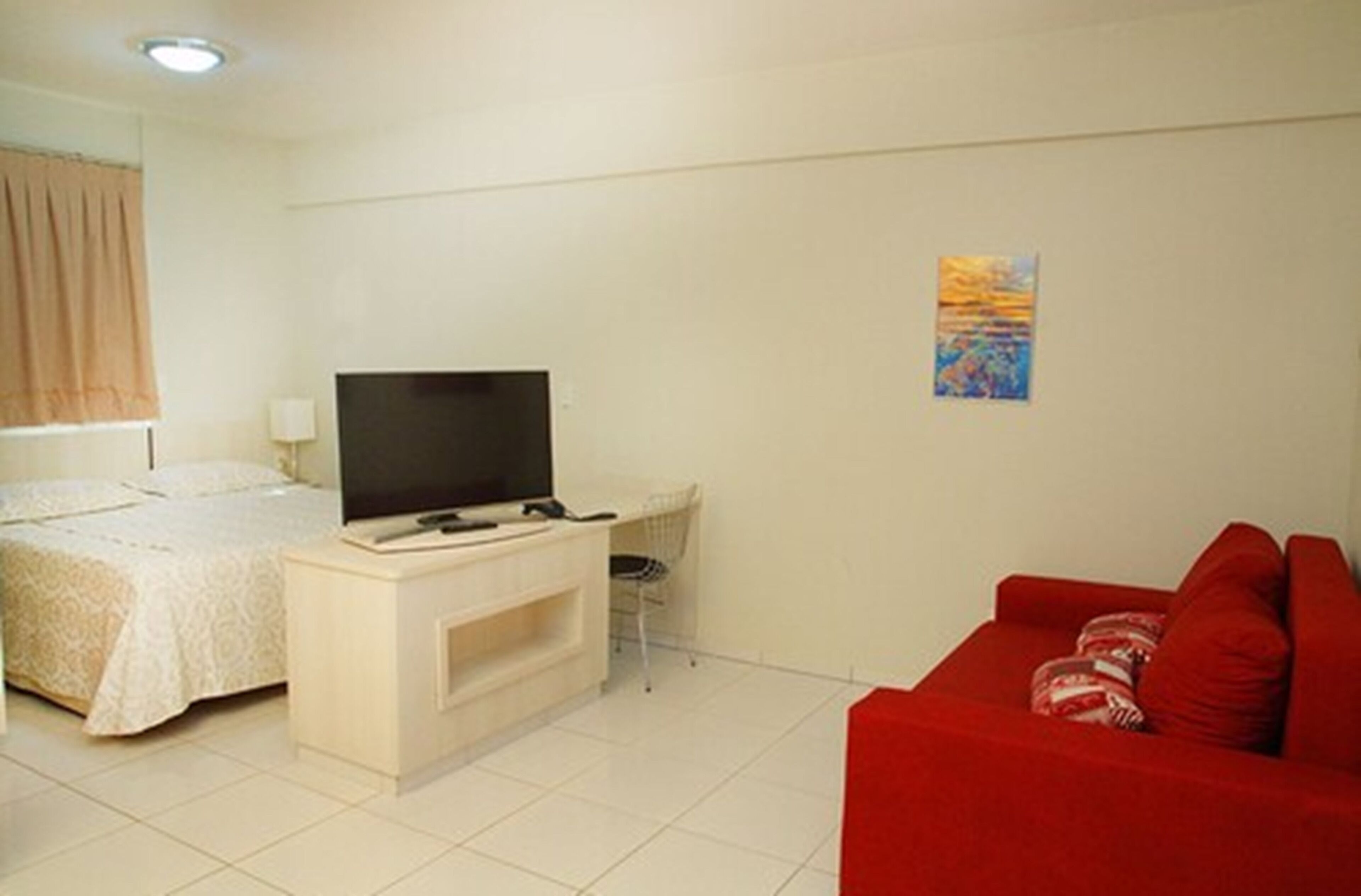A hotel room with a bed, a TV on a stand, a red sofa, and a small desk with a chair.