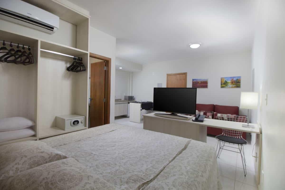 Um quarto com cama, escrivaninha, televisão e armário.