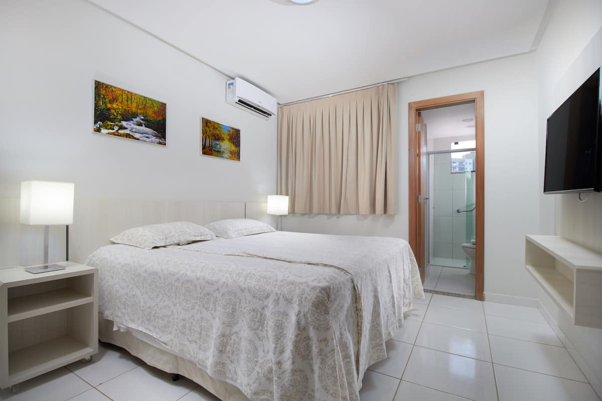 Quarto com cama, mesas de cabeceira, televisão e obras de arte na parede.