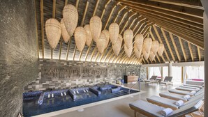 Um spa moderno com uma grande piscina interior, vigas de madeira no teto e áreas de estar iluminadas pelo sol.