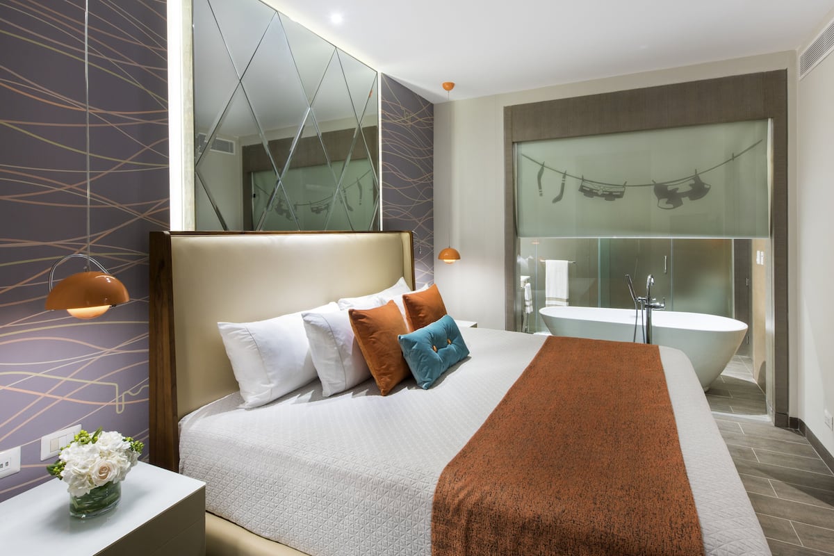 Ein modernes Hotelzimmer mit einem großen Bett, einem Badezimmer mit Badewanne und einem Spiegel über dem Bett.