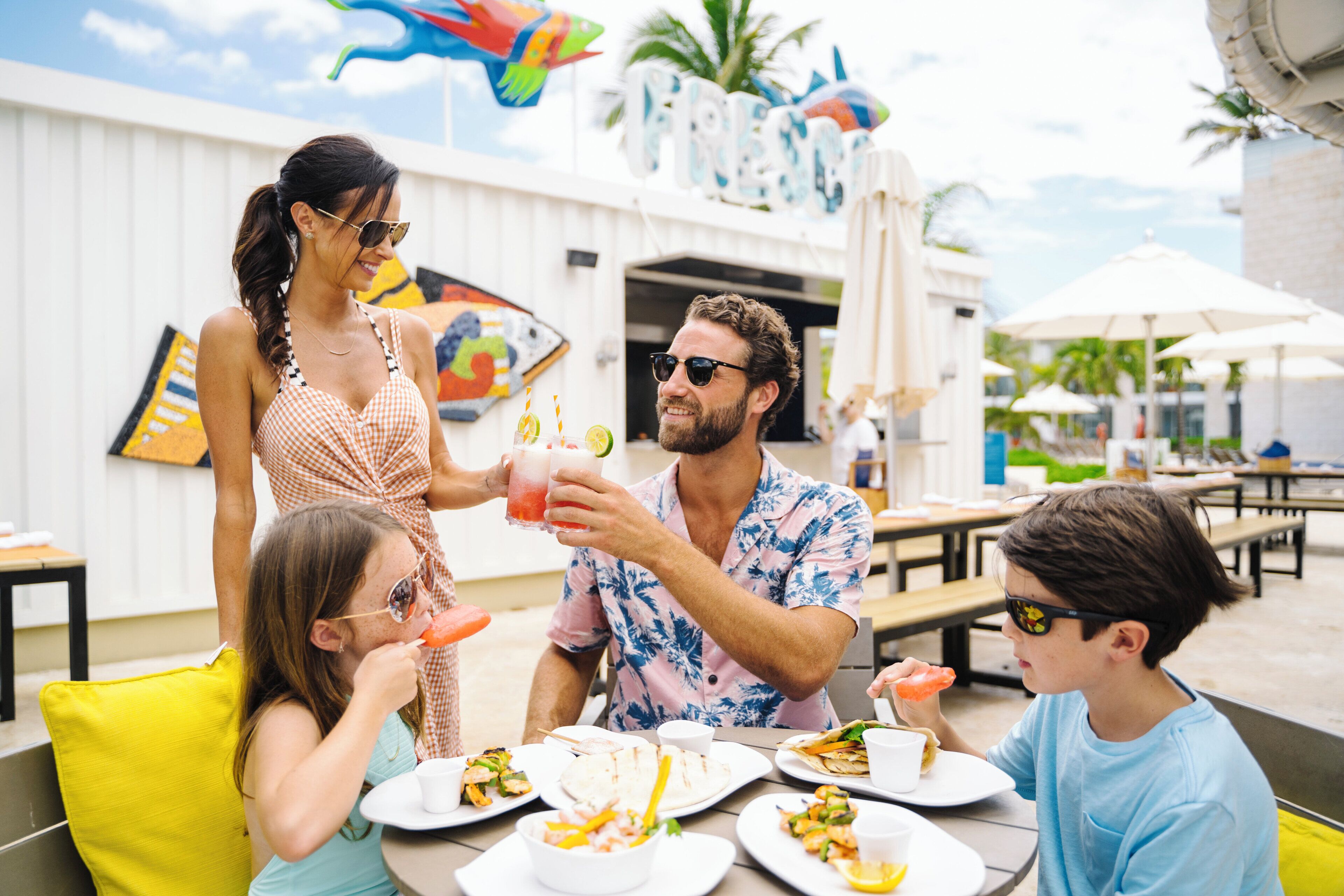 Un grupo de personas cenando al aire libre en un restaurante con fachada blanca y decoraciones coloridas.