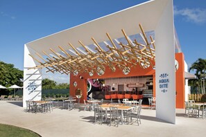 An outdoor dining area with tables and chairs, a large white structure with orange accents, and a sign that reads "AQUA BITE".