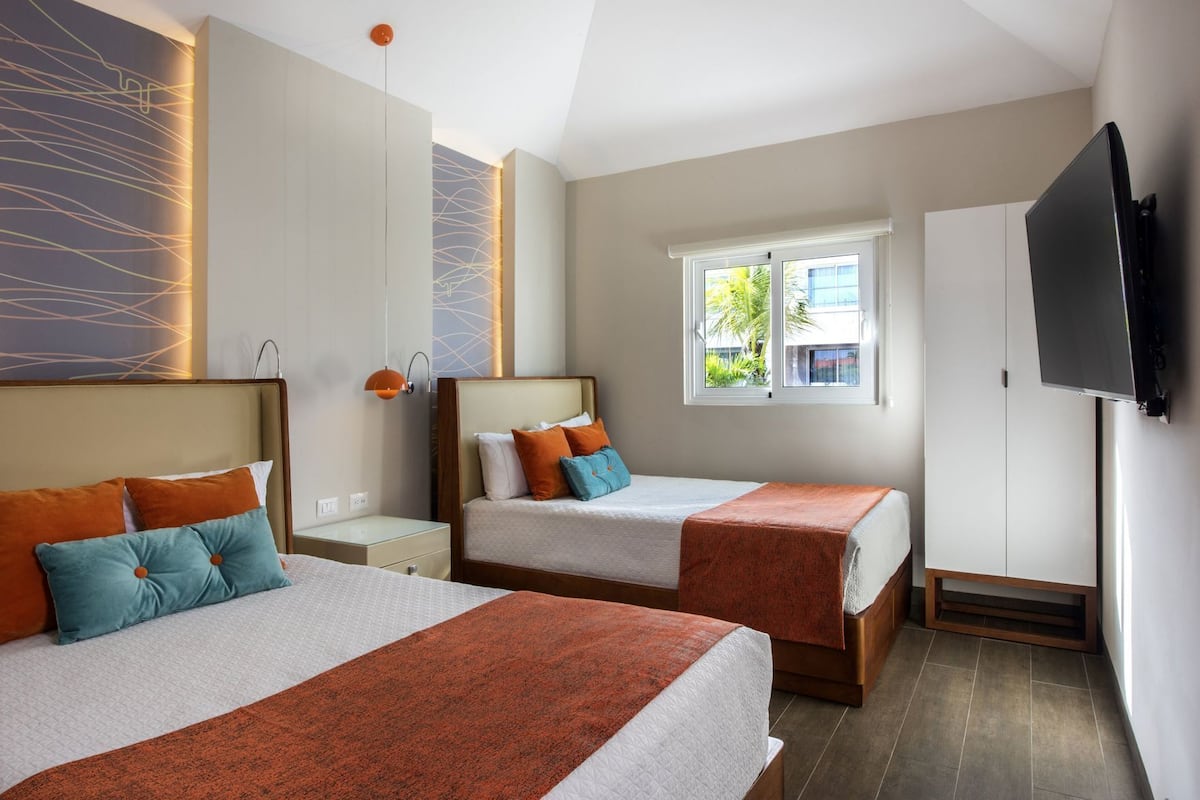 Ein Hotelzimmer mit zwei Betten, einem Fernseher, einem Kleiderschrank und einem Fenster mit Aussicht.