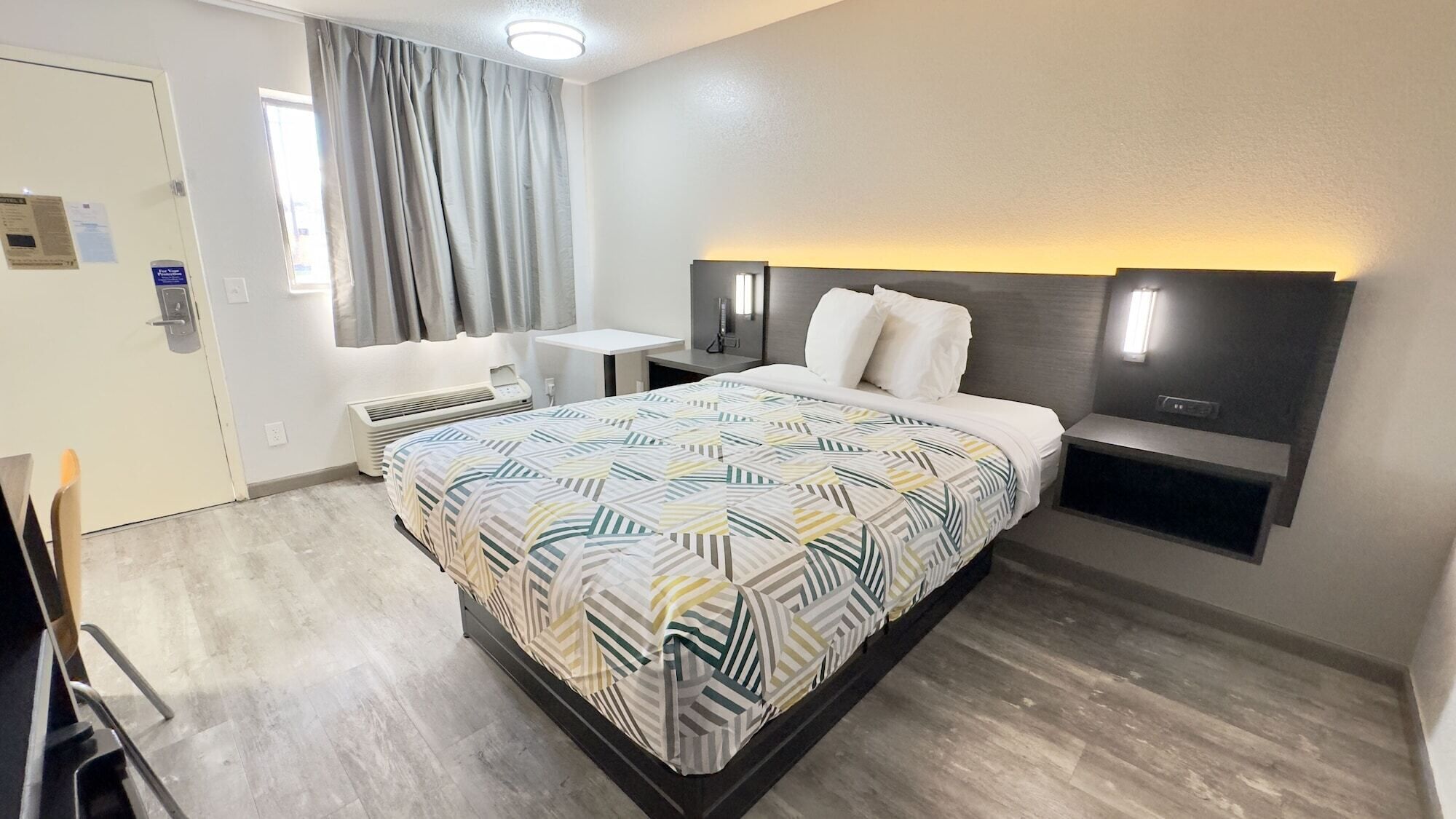 Una habitación de hotel moderna con una cama grande, una mesita de noche, un escritorio pequeño y una silla.