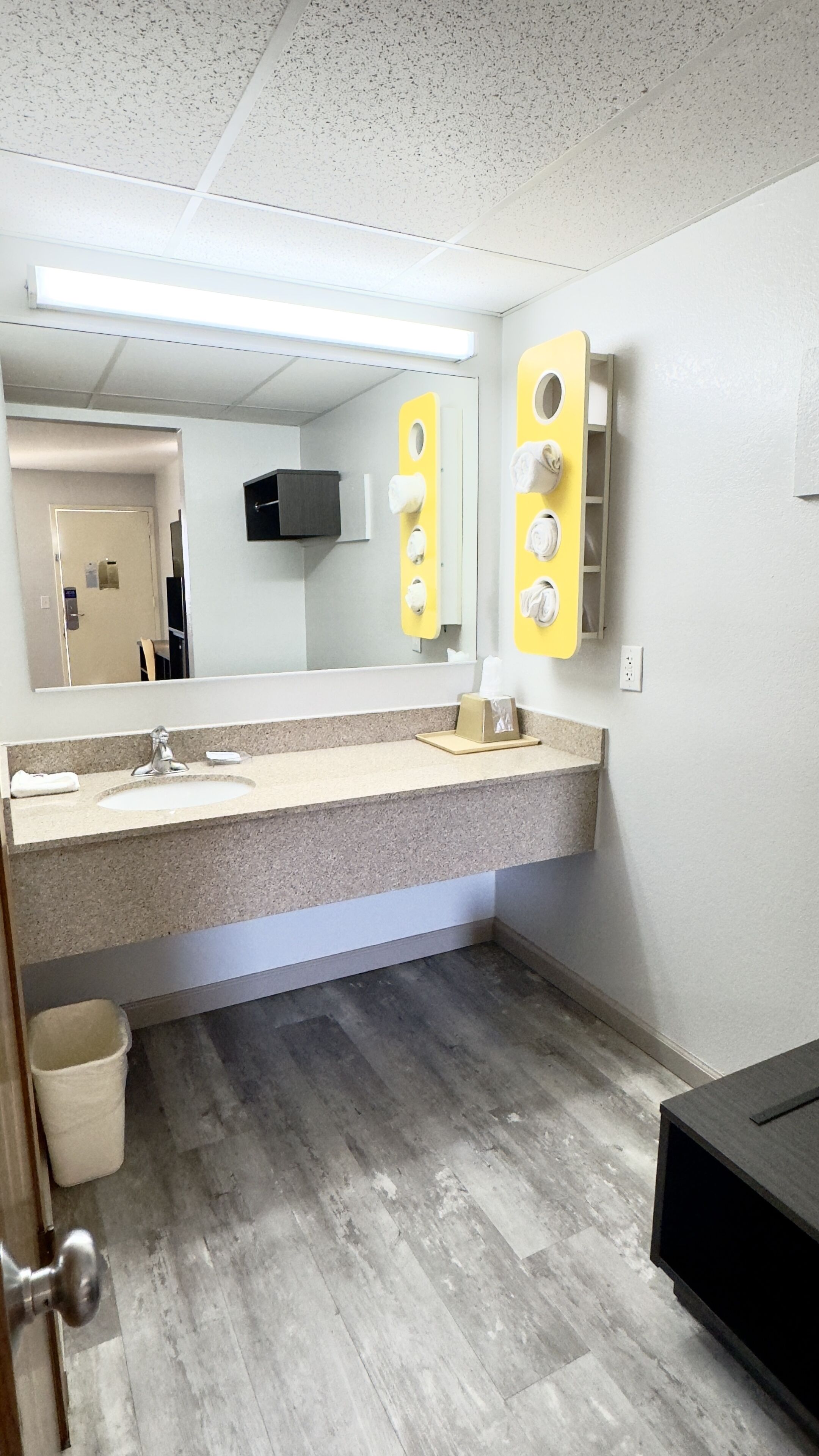 A bathroom with a granite countertop, a mirror, a towel dispenser, and a trash bin.