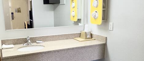 A bathroom with a granite countertop, a mirror, a towel dispenser, and a trash bin.