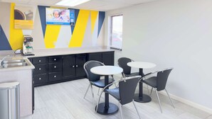 A modern kitchen area with a coffee machine, a sink, and a trash bin. There are four black chairs around two white round tables. - Motel 6 Dyersburg, TN (Dyersburg)