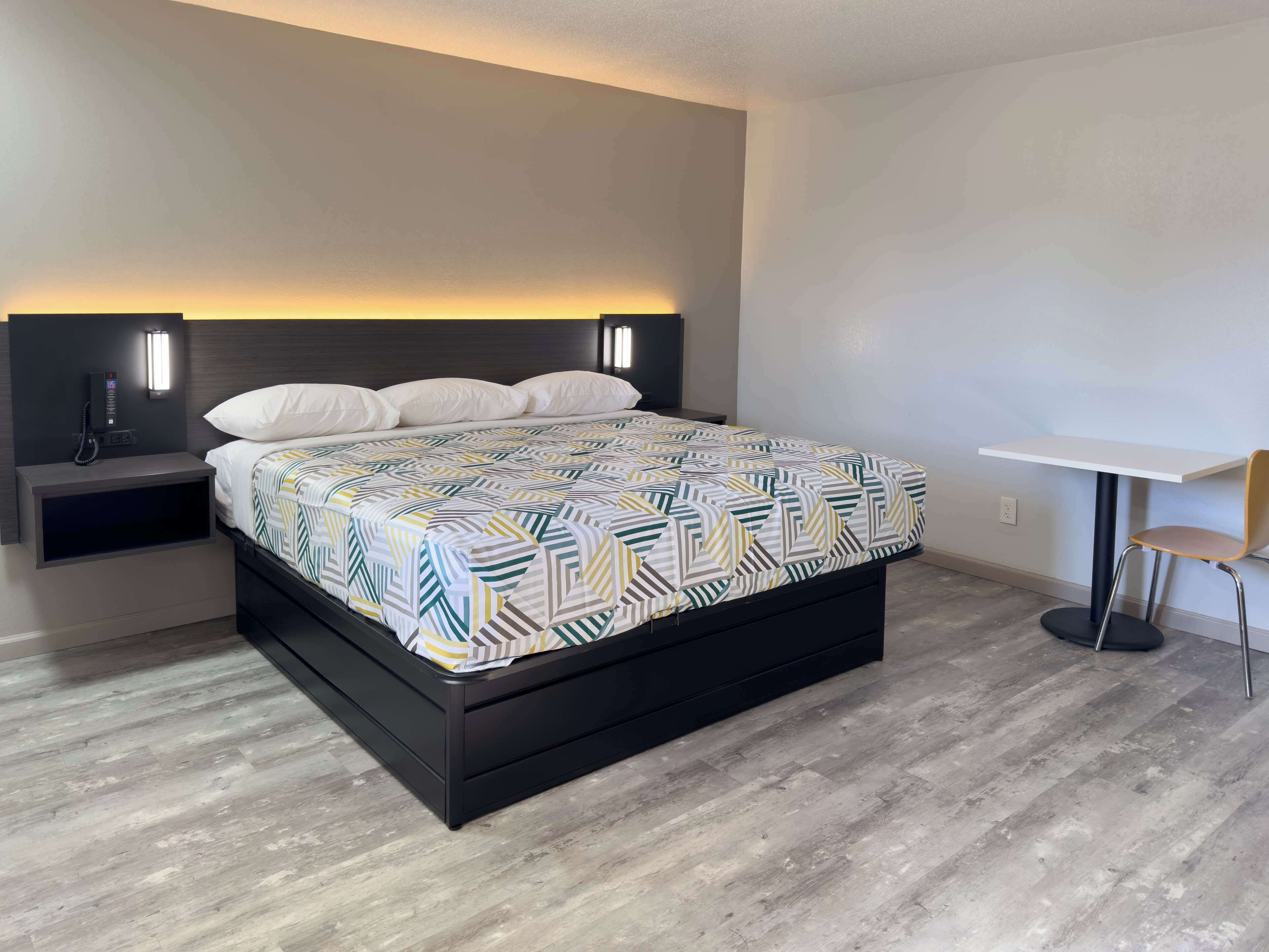 Un dormitorio moderno con una cama, mesitas de noche y una pequeña mesa con una silla.