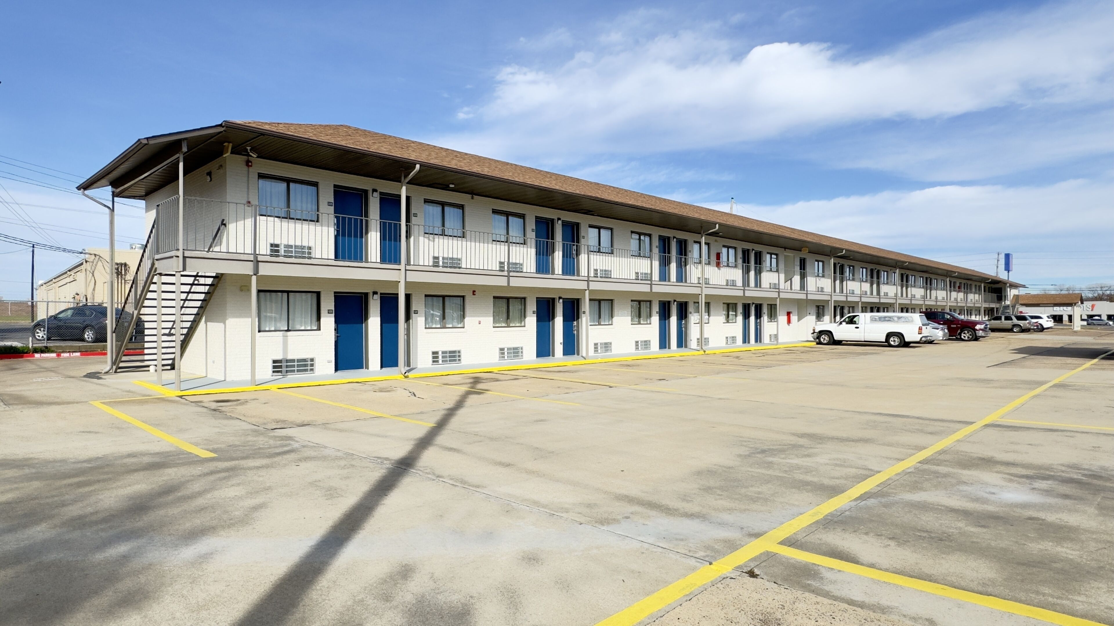 Ein Motel mit zweistöckigem Bau, einem überdachten Parkbereich und blauem Himmel.