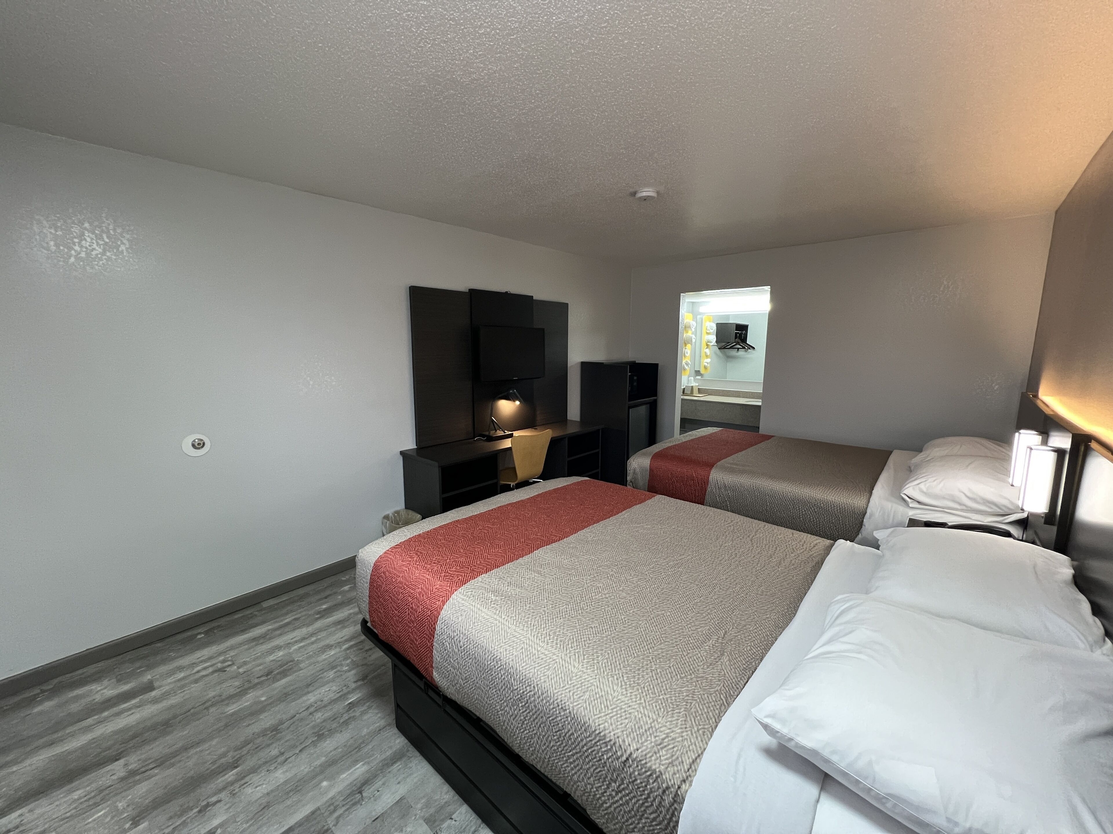 Quarto de hotel com duas camas, uma mesa, uma cadeira, uma televisão e um espelho.