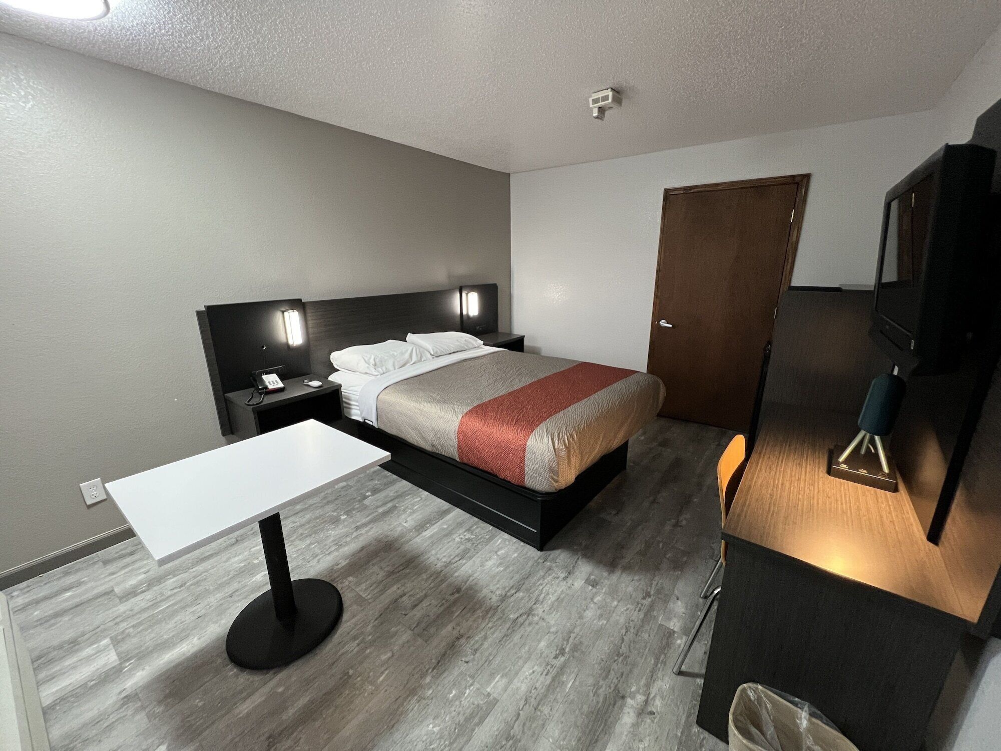 A modern hotel room with a bed, bedside table, lamp, and a TV stand.