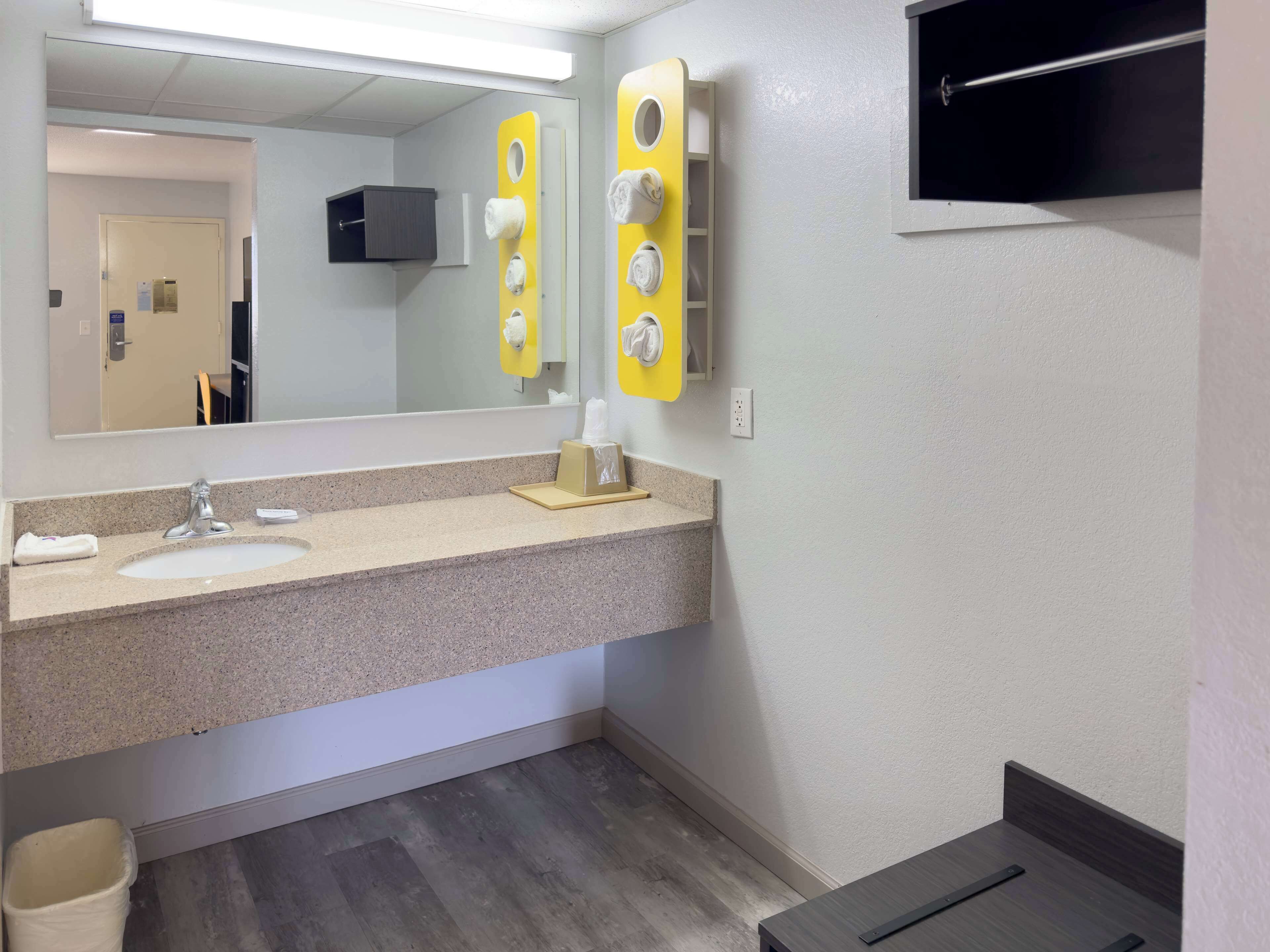 A bathroom with a granite countertop, a sink, a mirror, and a towel dispenser.