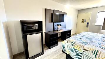 Habitación de hotel con cama, microondas, televisión y escritorio con lámpara.