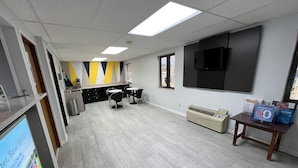 A modern office space with a kitchenette, two round tables with chairs, a large flat-screen TV, and a wall-mounted air conditioner. - Motel 6 Dyersburg, TN (Dyersburg)