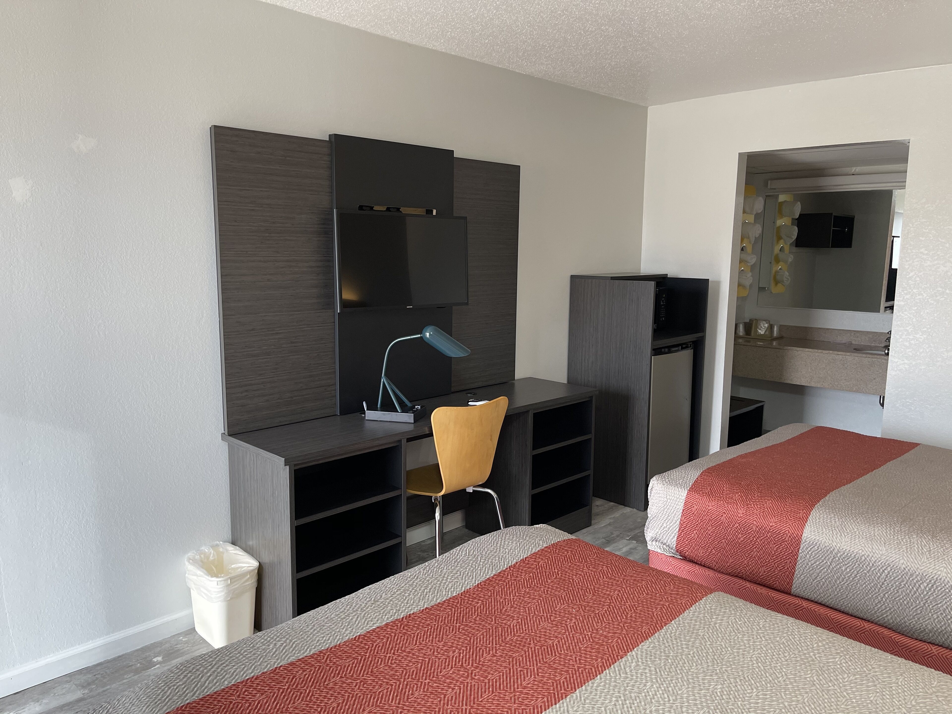 A hotel room with a bed, a desk with a chair, a TV, and a mirror.