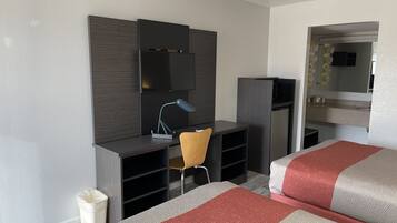 A hotel room with a bed, a desk with a chair, a TV, and a mirror.