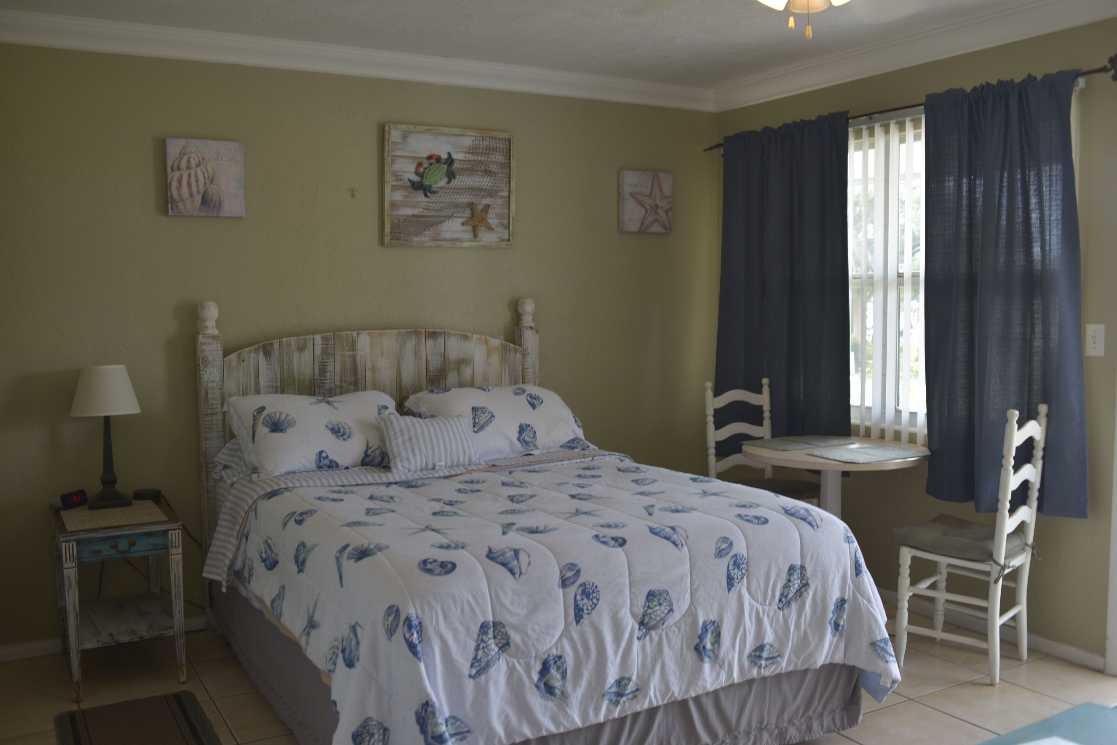 A bedroom with a bed, a nightstand, a chair, and a window with curtains.