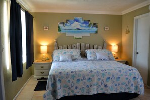 Un dormitorio con cama, dos mesitas de noche, una mesita auxiliar, un cuadro en la pared y una puerta.