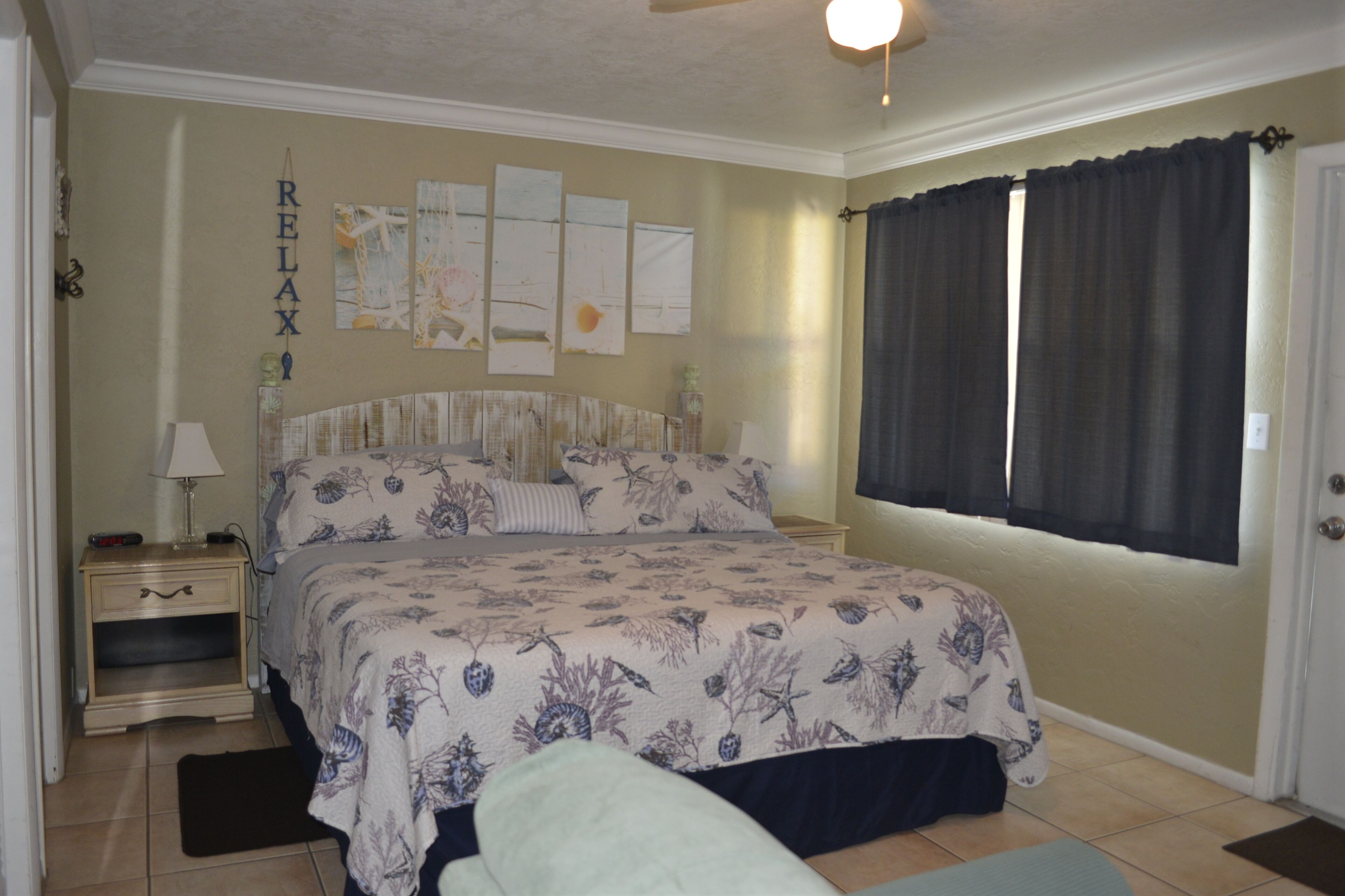 A bedroom with a bed, a nightstand, a lamp, a window with curtains, and wall art.