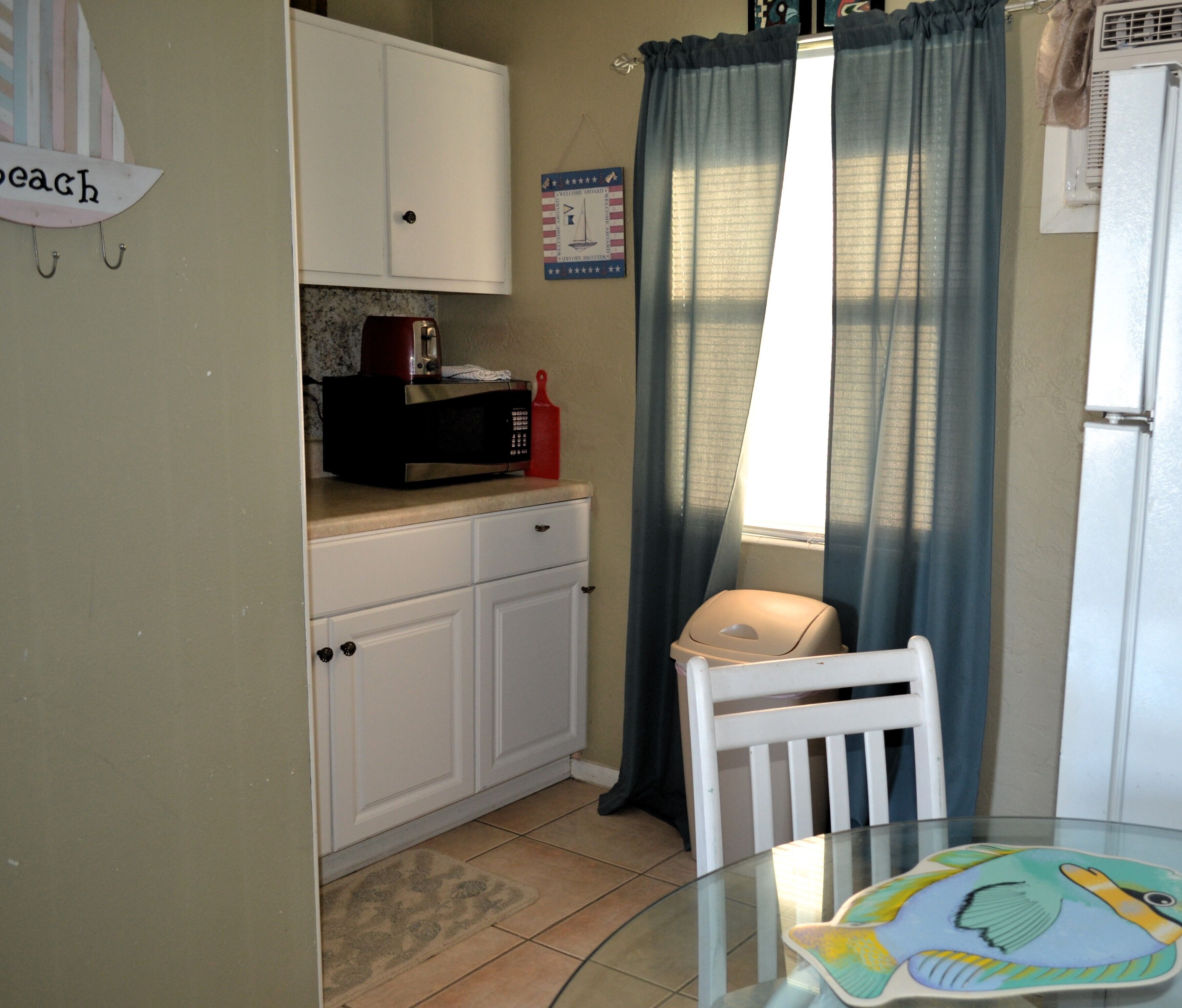 A compact kitchen with white cabinets, a microwave, a toaster, and a small table with a placemat.